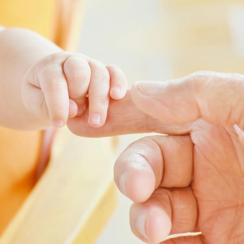 A baby's hand gently grabbing an adult's finger
